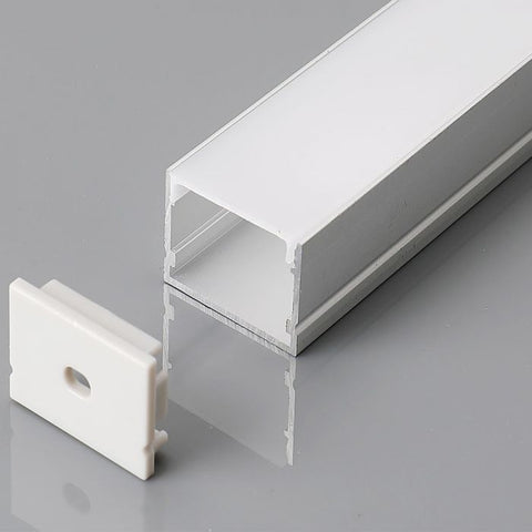 A close-up shot of a silver LED profile with a milky white diffuser cover and a white end cap on a grey reflective surface.