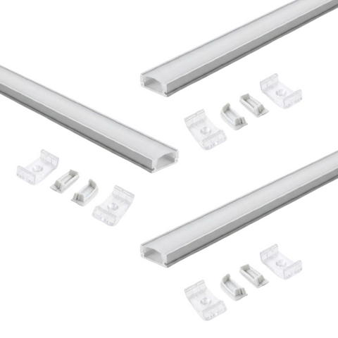 Three sets of aluminium profiles with a white finish and white diffuser covers laid on a white surface with two mounting brackets and end caps for each profile.
