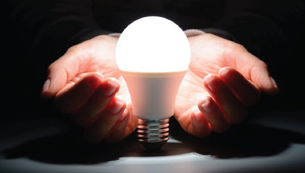 A man with his hands out resting underneath a lightbulb