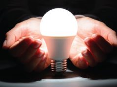 A man with his hands out resting underneath a lightbulb