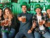 5 people wearing green hats and holding beers