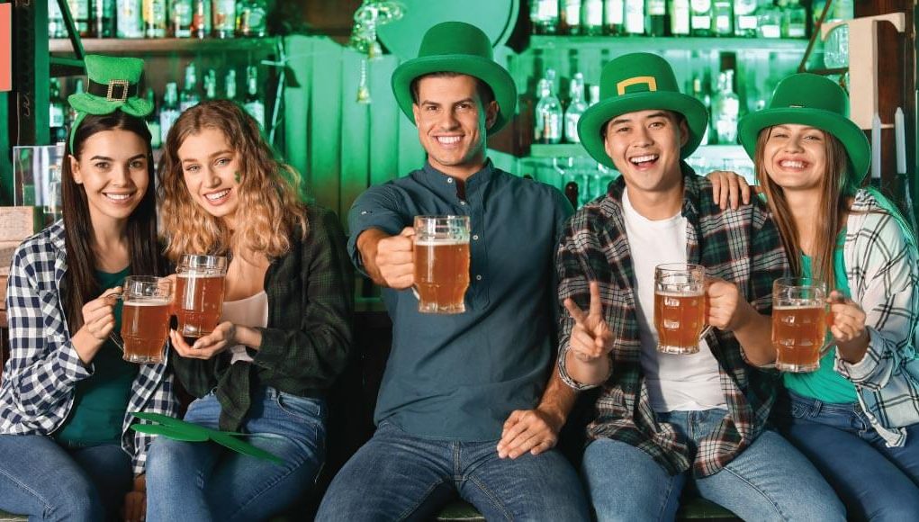 5 people wearing green hats and holding beers