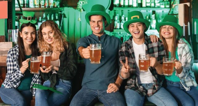 5 people wearing green hats and holding beers