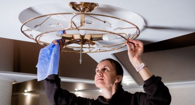 woman cleaning ceiling light fixture
