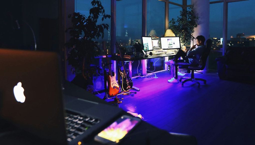 laptop foreground with man sitting by his desk in background