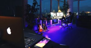 laptop foreground with man sitting by his desk in background