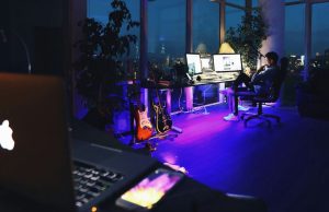 laptop foreground with man sitting by his desk in background