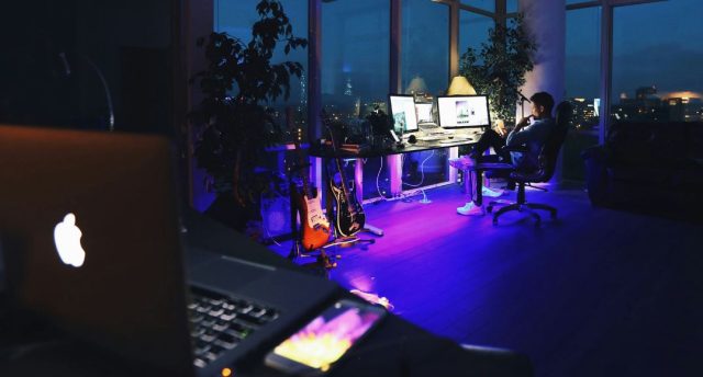 laptop foreground with man sitting by his desk in background