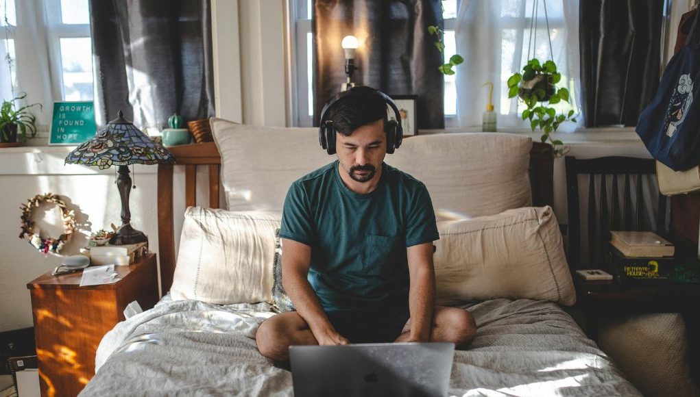 man with a laptop in the bedroom on his bed working