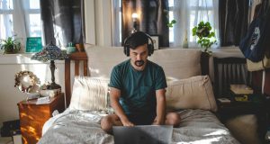 man with a laptop in the bedroom on his bed working