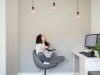 Woman sitting on a swivel chair looking up at three lit light bulbs