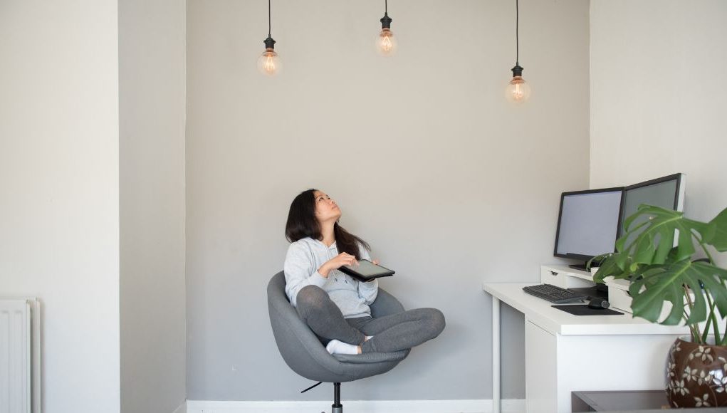 Woman sitting on a swivel chair looking up at three lit light bulbs