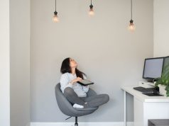 Woman sitting on a swivel chair looking up at three lit light bulbs