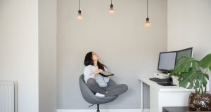 Woman sitting on a swivel chair looking up at three lit light bulbs