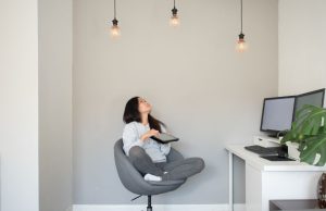 Woman sitting on a swivel chair looking up at three lit light bulbs