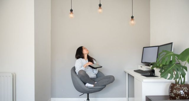 Woman sitting on a swivel chair looking up at three lit light bulbs