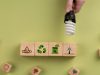 Hand holding a CFL lamp over some blocks with different symbols related to recycling.