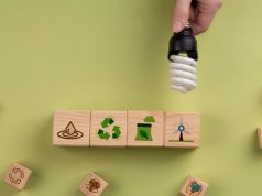 Hand holding a CFL lamp over some blocks with different symbols related to recycling.
