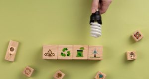 Hand holding a CFL lamp over some blocks with different symbols related to recycling.