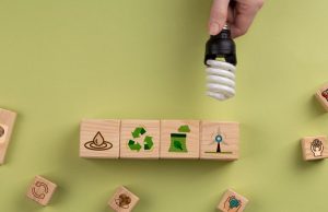 Hand holding a CFL lamp over some blocks with different symbols related to recycling.