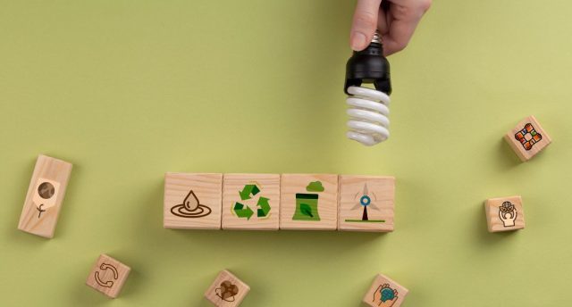 Hand holding a CFL lamp over some blocks with different symbols related to recycling.