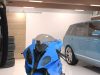 A well-lit garage with a blue car and motorcycle and multiple batten lights on the ceiling.