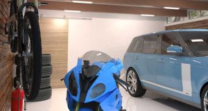 A well-lit garage with a blue car and motorcycle and multiple batten lights on the ceiling.