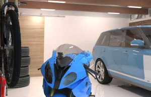 A well-lit garage with a blue car and motorcycle and multiple batten lights on the ceiling.