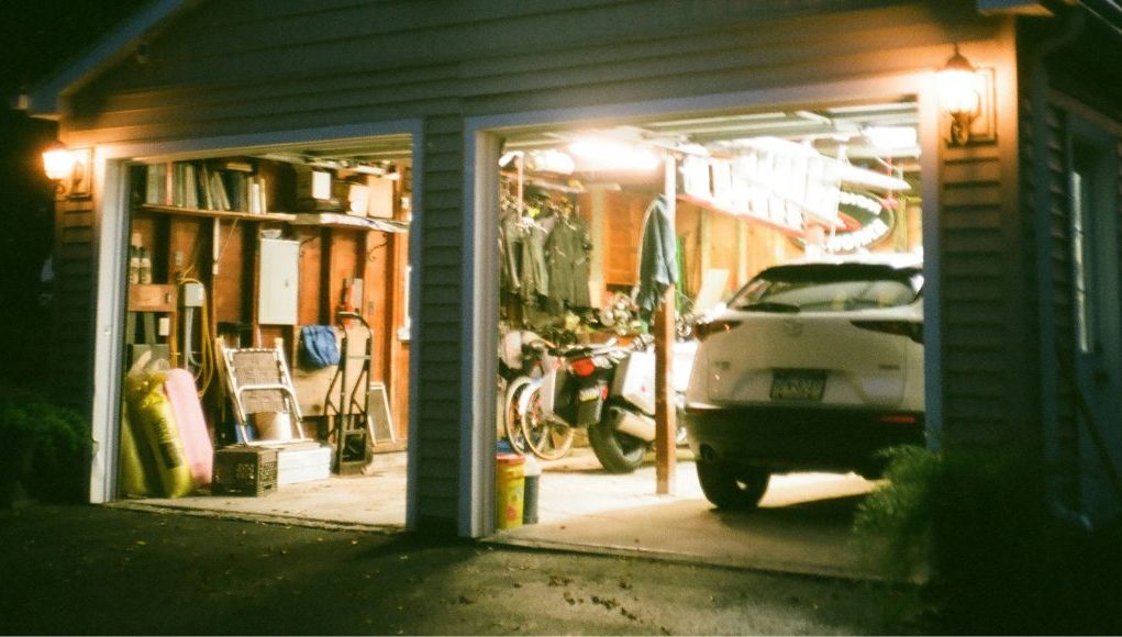 An open garage with lights on and a visible car and a variety of garage items.