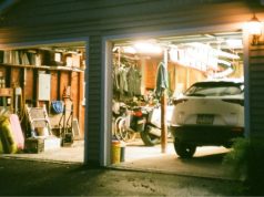 An open garage with lights on and a visible car and a variety of garage items.