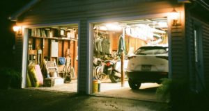 An open garage with lights on and a visible car and a variety of garage items.