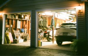 An open garage with lights on and a visible car and a variety of garage items.
