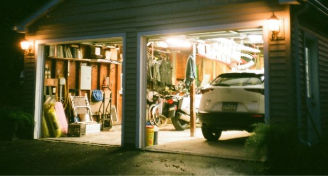 An open garage with lights on and a visible car and a variety of garage items.