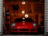 Front of an open garage showing a red car and a dim interior with a few warm lights.