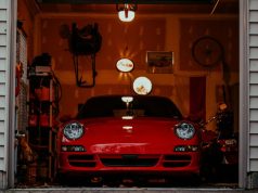 Front of an open garage showing a red car and a dim interior with a few warm lights.