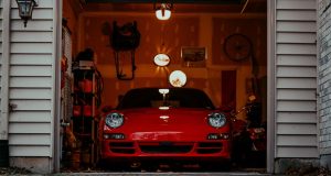 Front of an open garage showing a red car and a dim interior with a few warm lights.