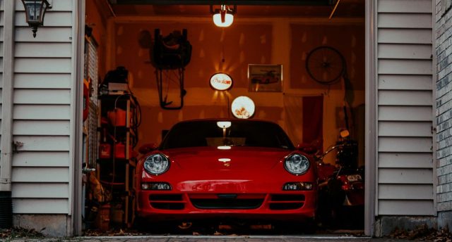 Garage Makeover Lighting Ideas for a Stylish, Functional Space Front of an open garage showing a red car and a dim interior with a few warm lights.