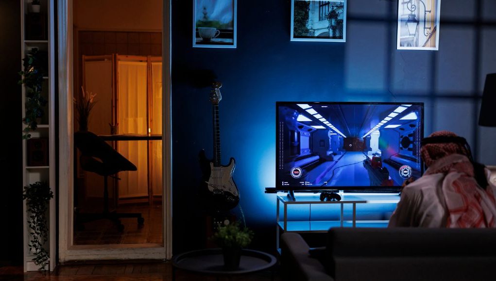 A person gaming in a dark room, his screen has a blue backlighting.