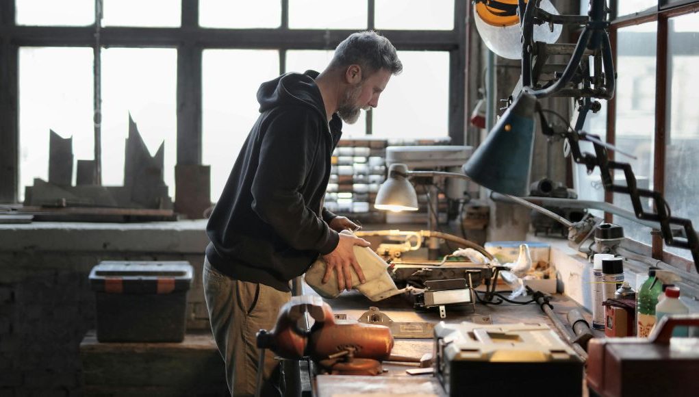 A man working on his working table in a garage with a warm desk light illuminating his work area.