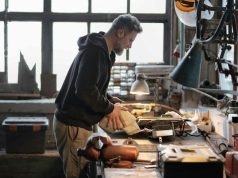 A man working on his working table in a garage with a warm desk light illuminating his work area.