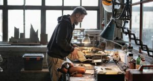 A man working on his working table in a garage with a warm desk light illuminating his work area.