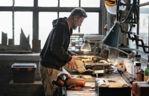 A man working on his working table in a garage with a warm desk light illuminating his work area.