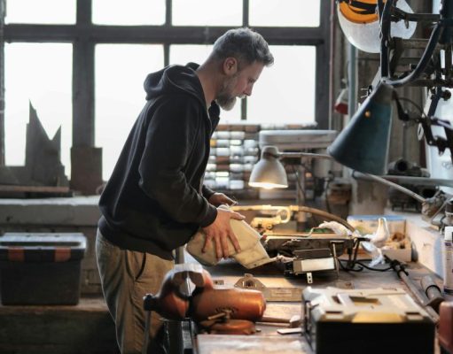 A man working on his working table in a garage with a warm desk light illuminating his work area.