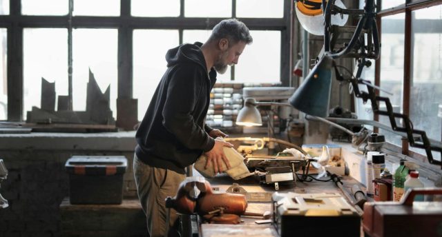 A man working on his working table in a garage with a warm desk light illuminating his work area.