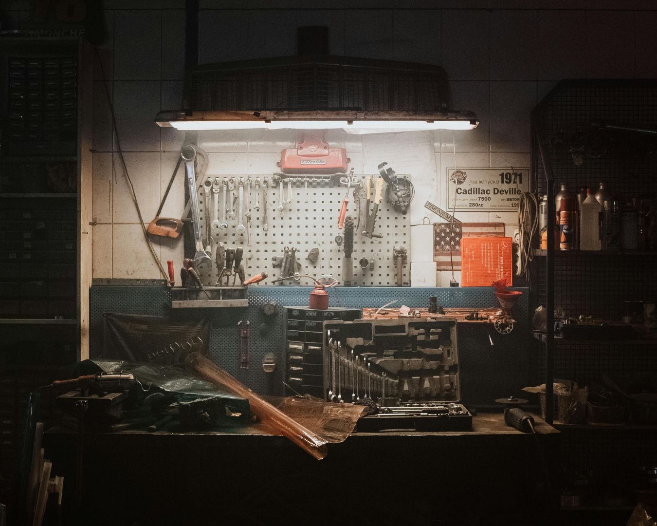 A working table lit by a single lamp. The table has tools on top of it and a lot more hanging on the wall.