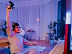 A man celebrating while holding a game console controller in a room lit with a blue and red light.