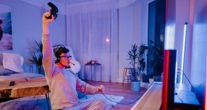 A man celebrating while holding a game console controller in a room lit with a blue and red light.