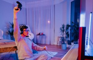 A man celebrating while holding a game console controller in a room lit with a blue and red light.