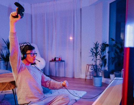 A man celebrating while holding a game console controller in a room lit with a blue and red light.