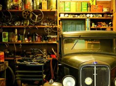 A garage interior basked in warm light and filled with a lot of trinkets and an old car on one side.